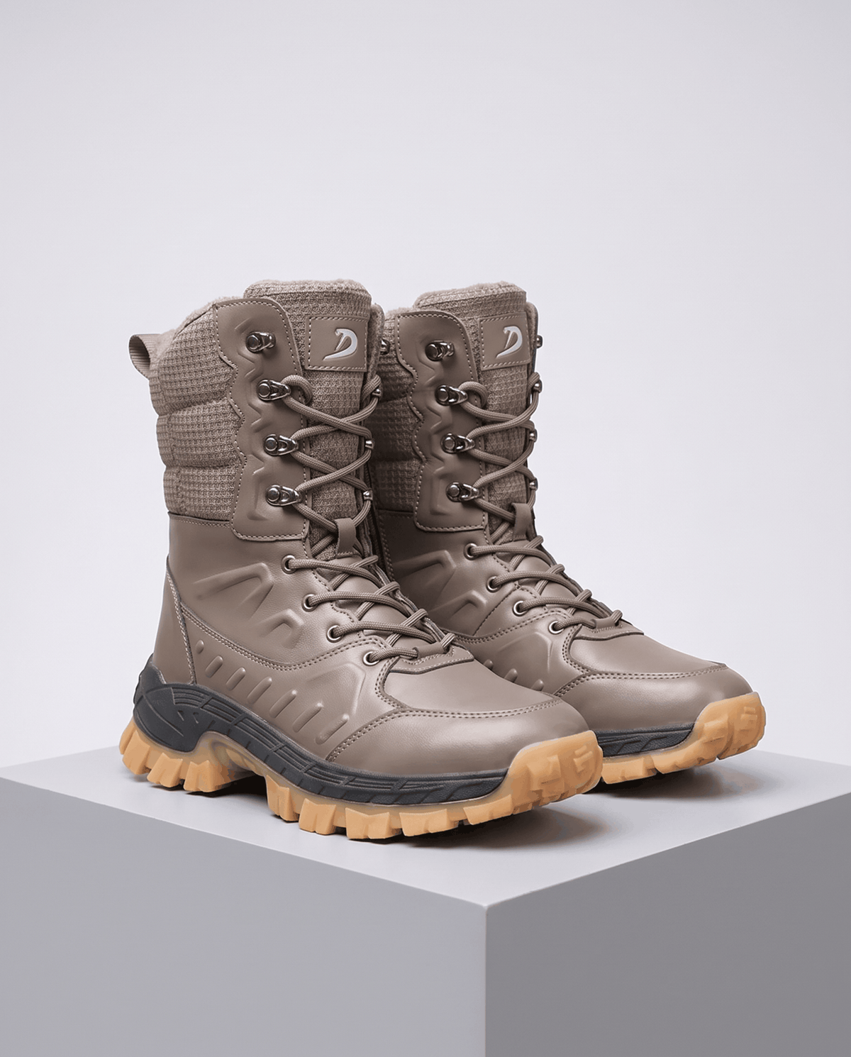 Khaki high-top snow boots with lace-up fronts and tan lug soles on a gray plinth