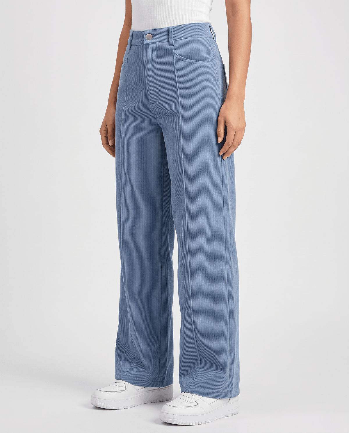 Woman wearing sky blue high-waisted corduroy wide-leg pants with white sneakers, angled front view