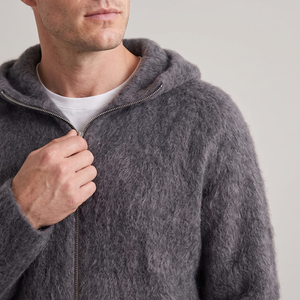 Close-up of a hand on the zip of the gray fuzzy hooded cardigan