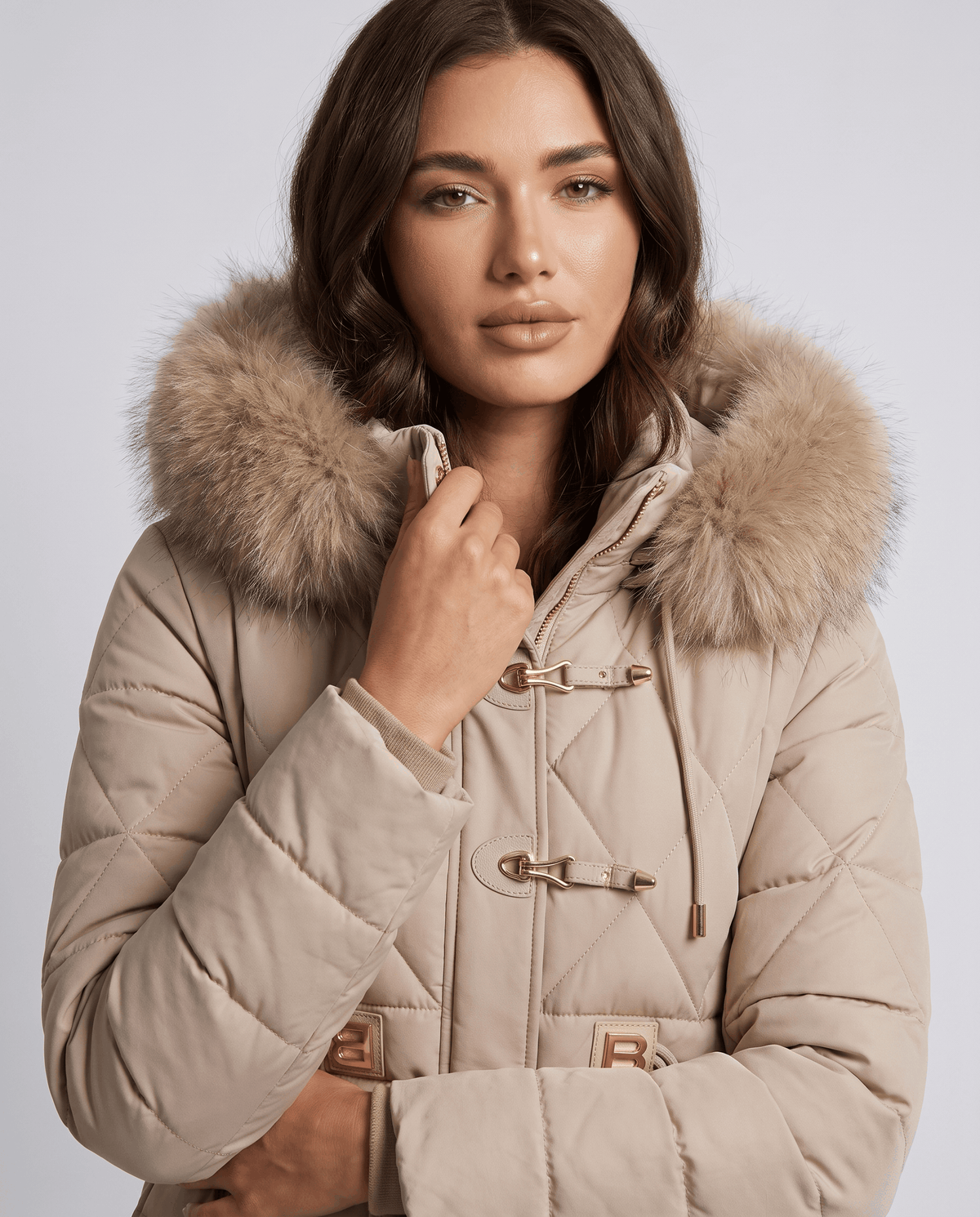 Model in beige jacket with plush-trim hood up and metal hook clasps at the front