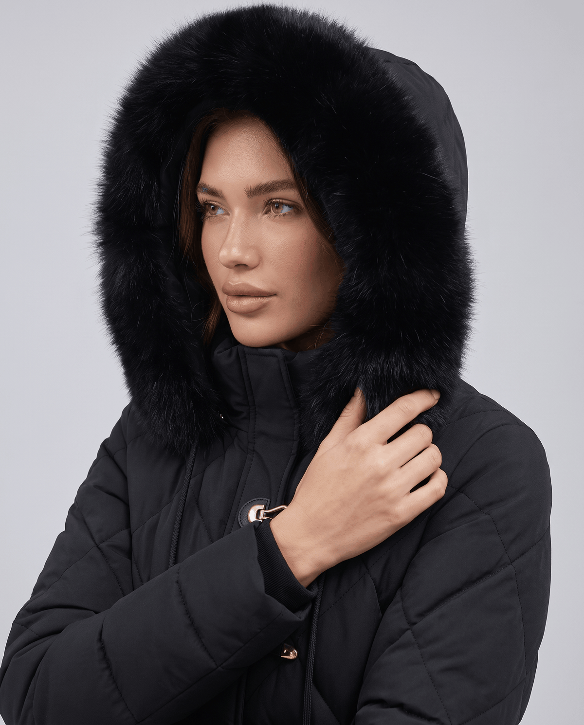 Close-up of model's face inside black plush-trim hood on quilted jacket
