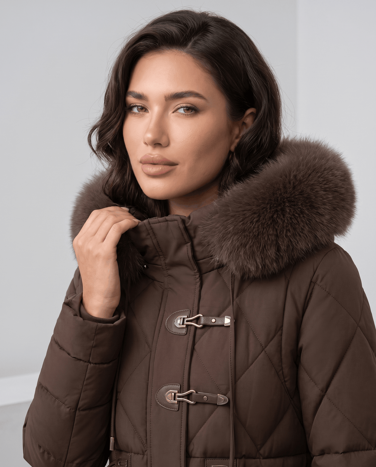 Model in brown jacket showing metal hook clasps and plush hood trim at the collar