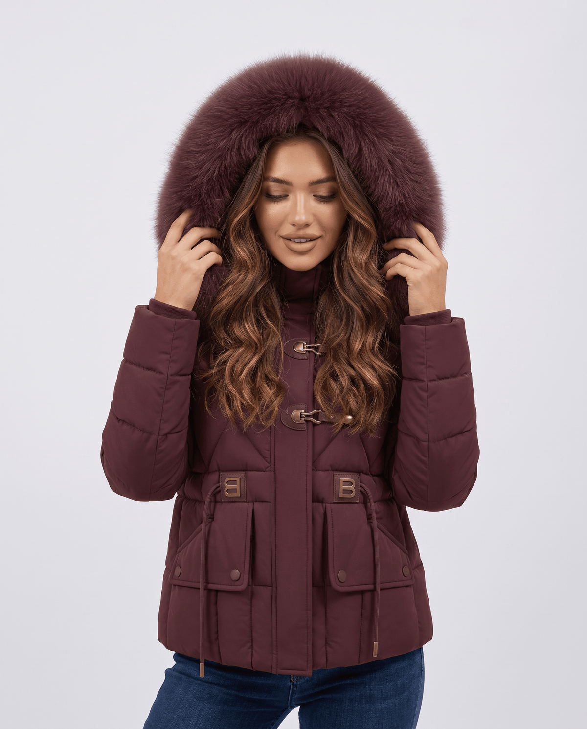 Woman wearing maroon hooded puffer jacket with plush-trim hood and cinched waist, front view