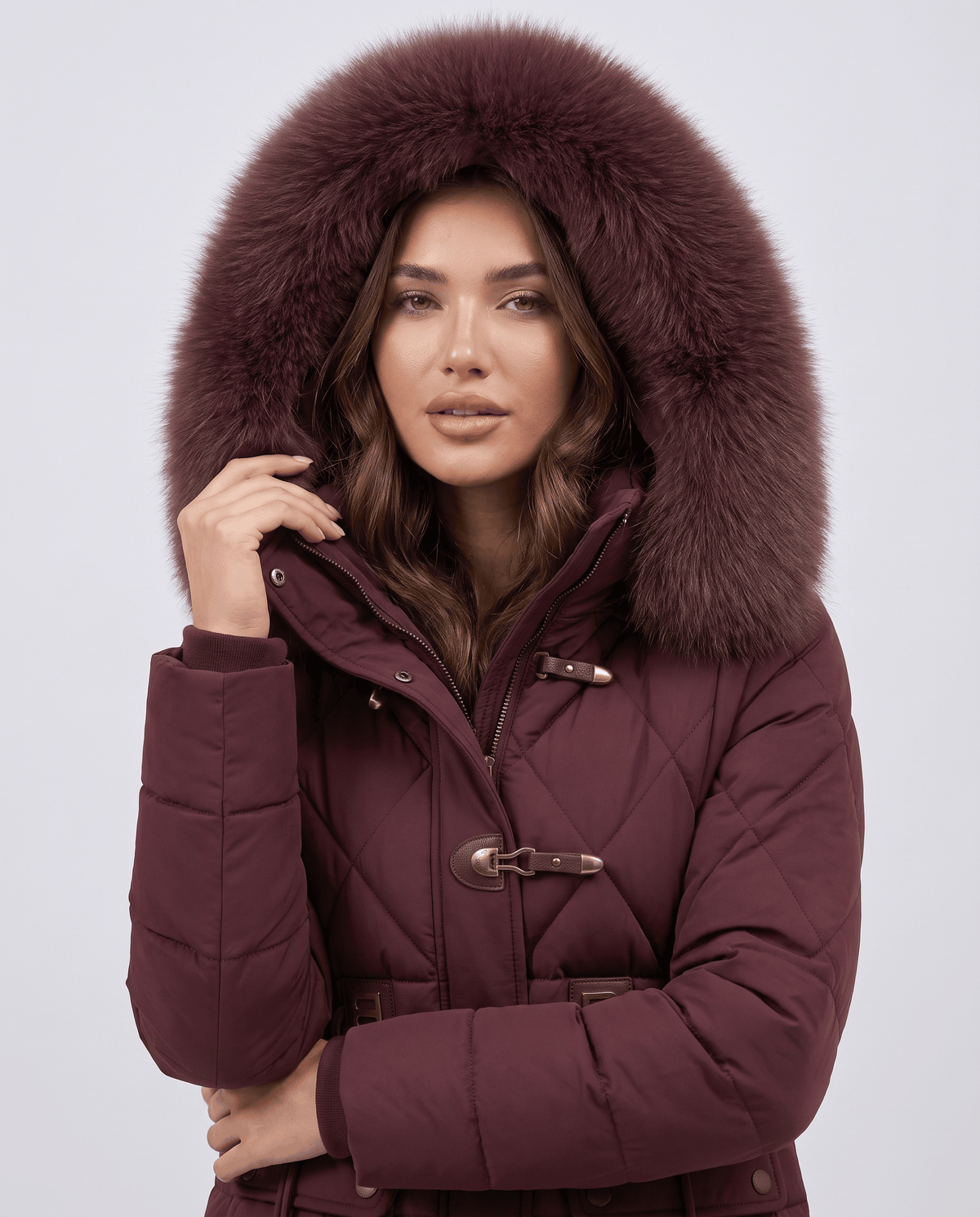 Model in maroon jacket with plush-trim hood up and hand resting at the collar