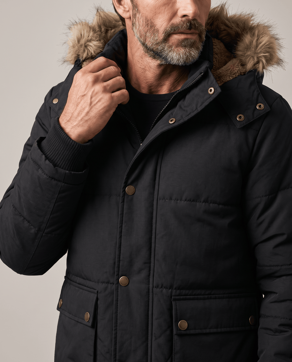 Man adjusting the collar of a black parka with fur-trim hood and snap pockets