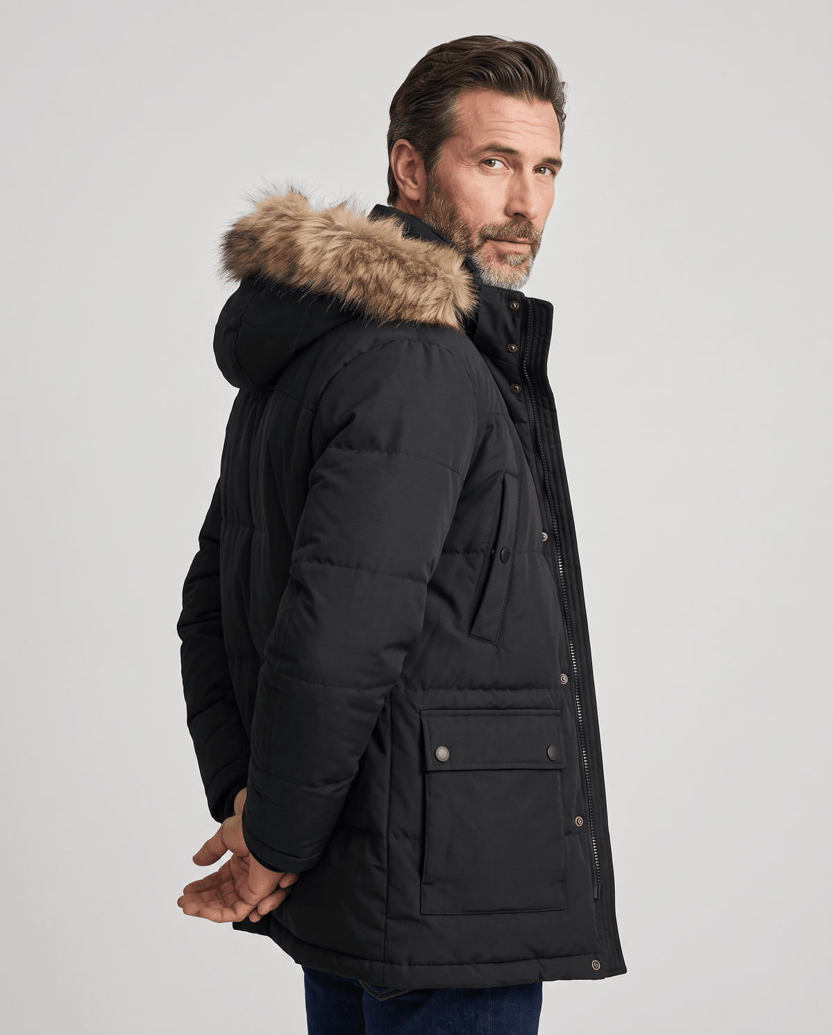Side view of black parka with fur-trim hood and front pocket worn over jeans