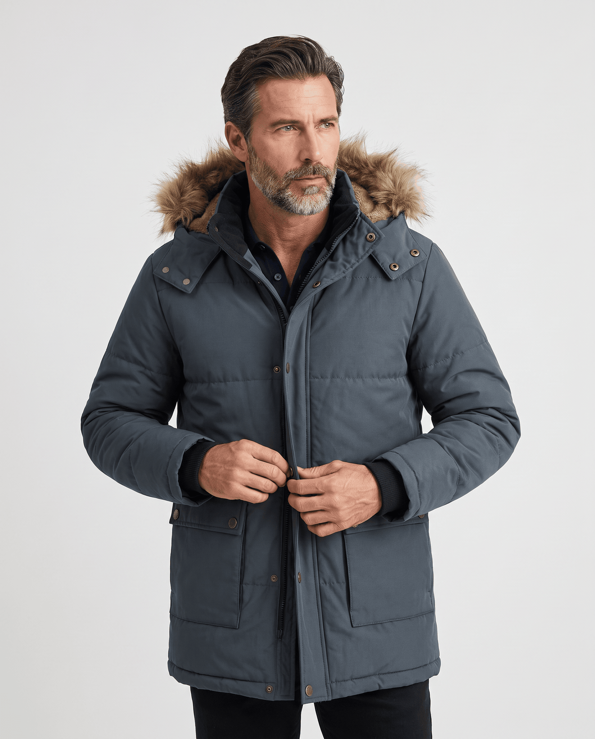Man wearing a dark blue hooded winter parka with fur-trim hood, hands at the front placket