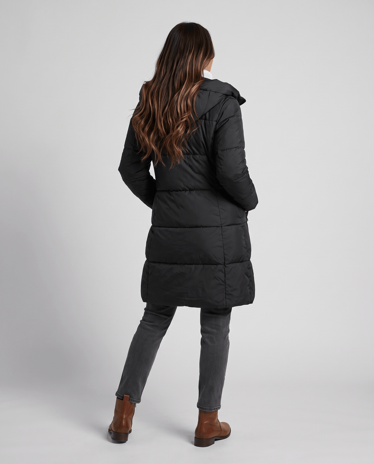 Back view of black quilted coat with brown ankle boots