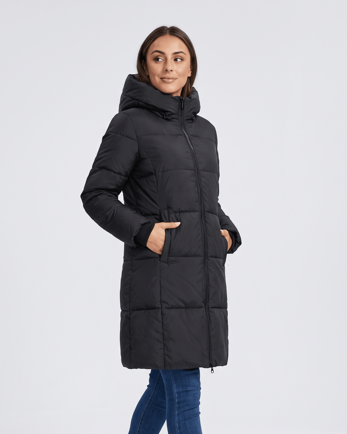 Woman in black knee-length puffer coat zipped up over blue jeans