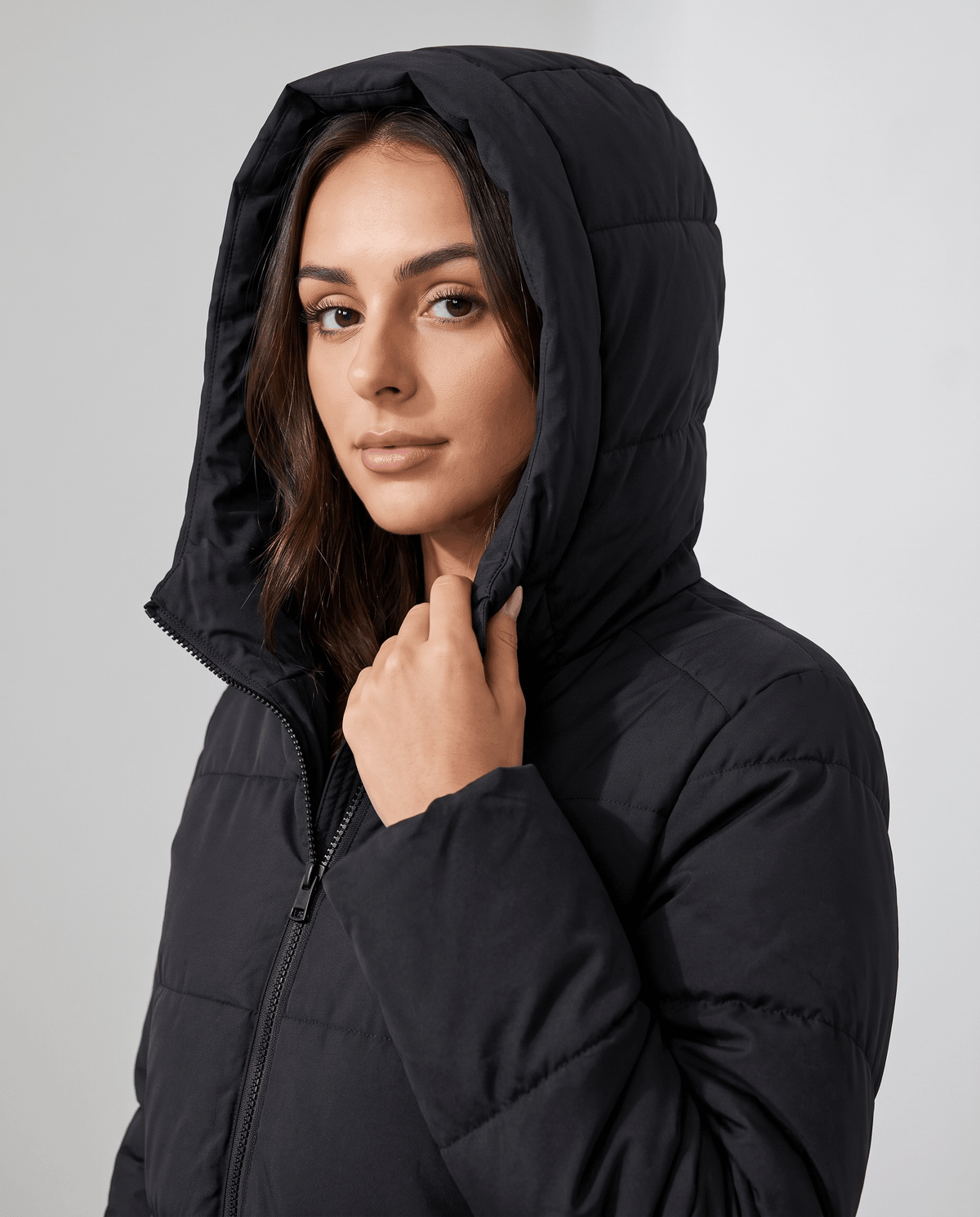 Model holding the hood of a black puffer coat close to her face