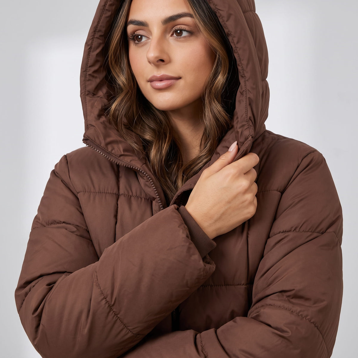 Model holding the hood of a dark brown puffer coat close to her face
