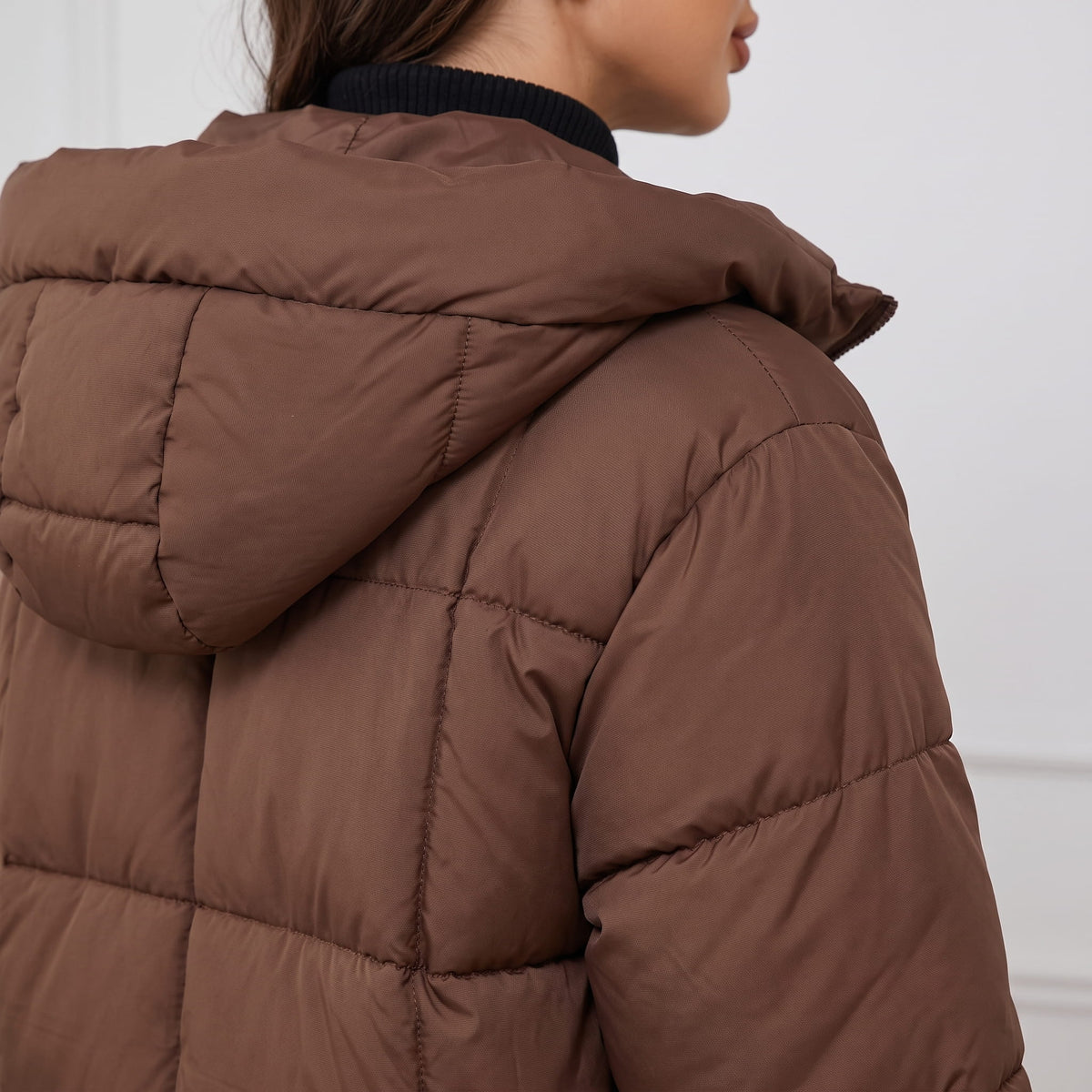Rear shoulder detail of dark brown coat showing hood and quilting