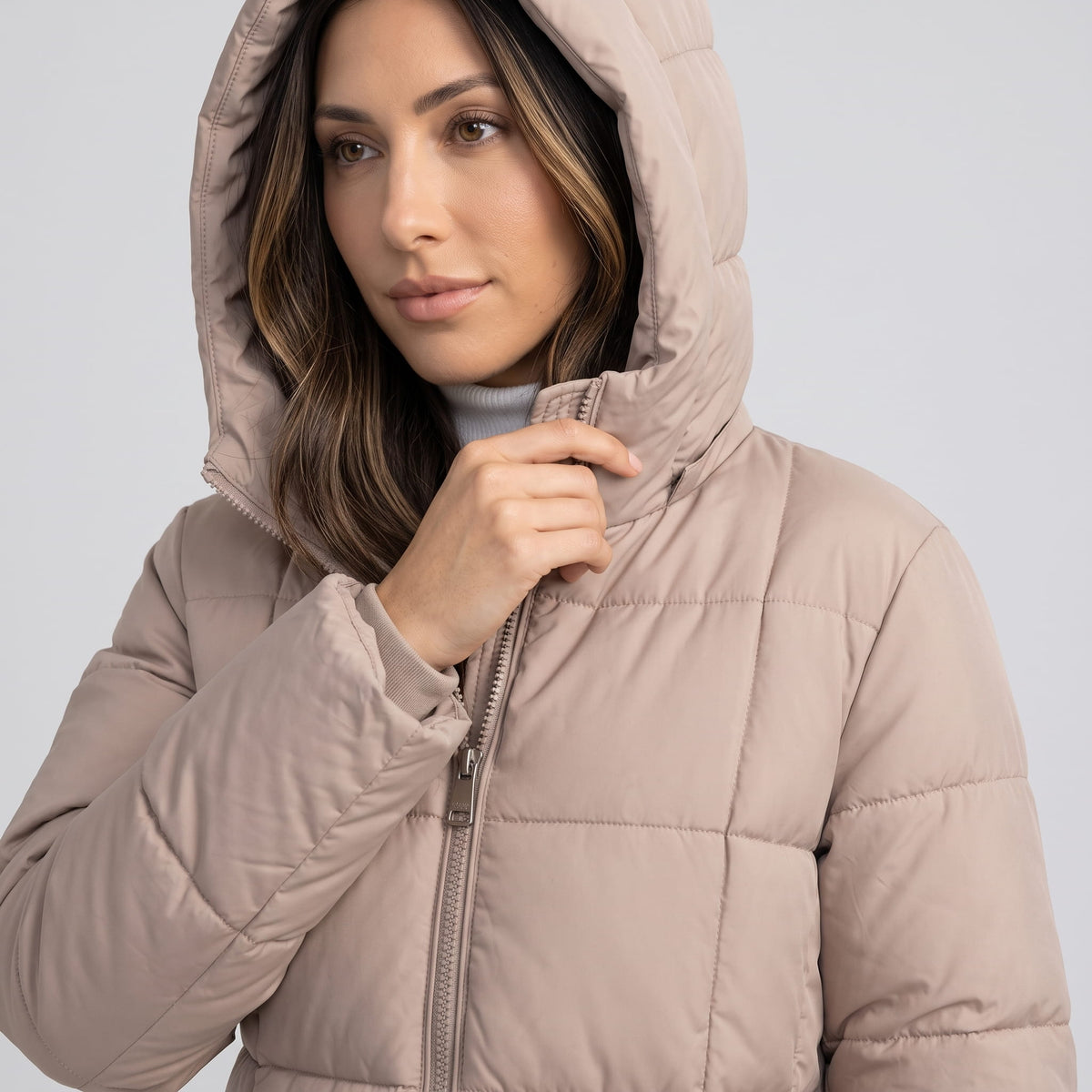 Model pulling the zip of a taupe coat with the hood up