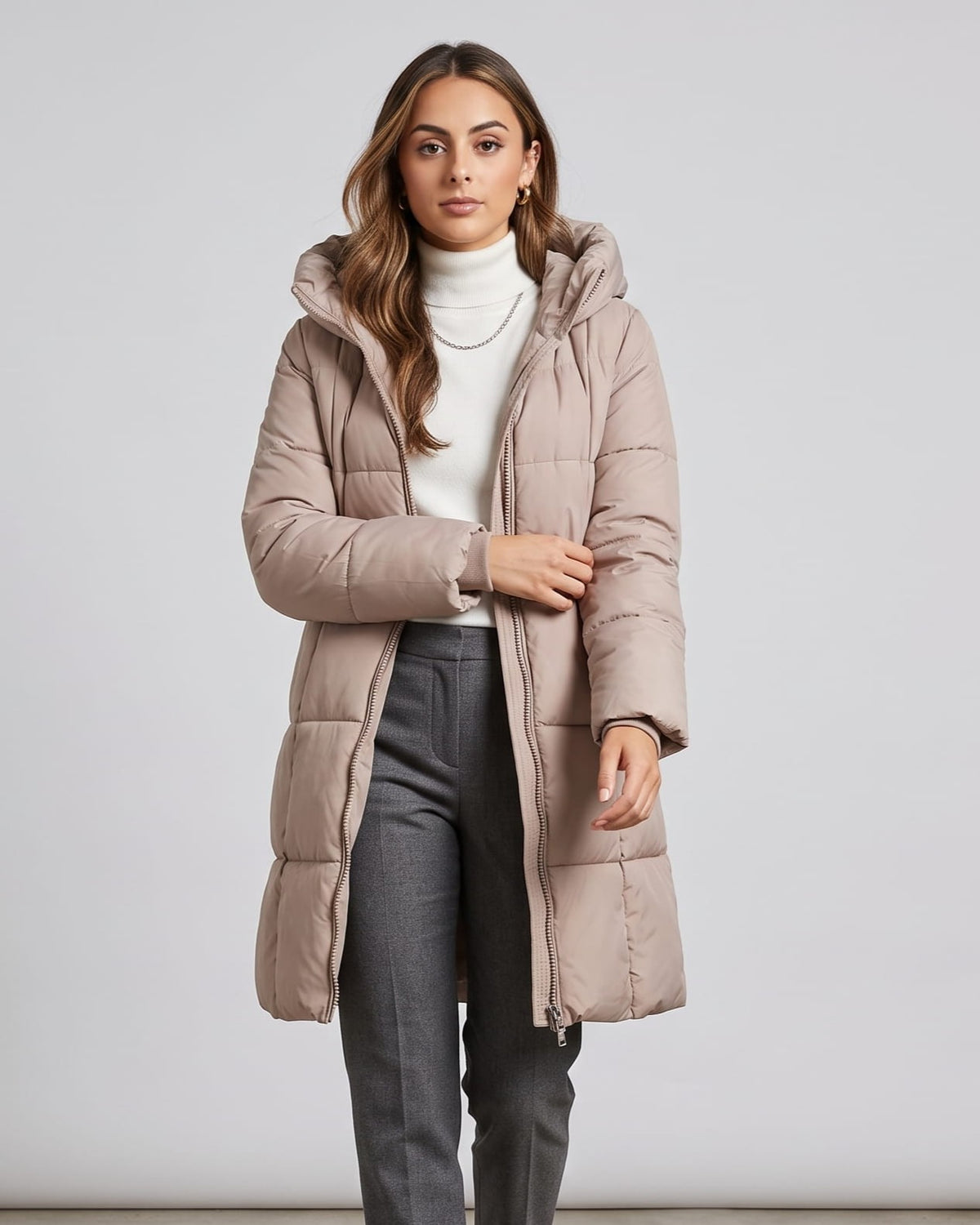 Woman in taupe knee-length puffer coat over a white turtleneck and gray jeans