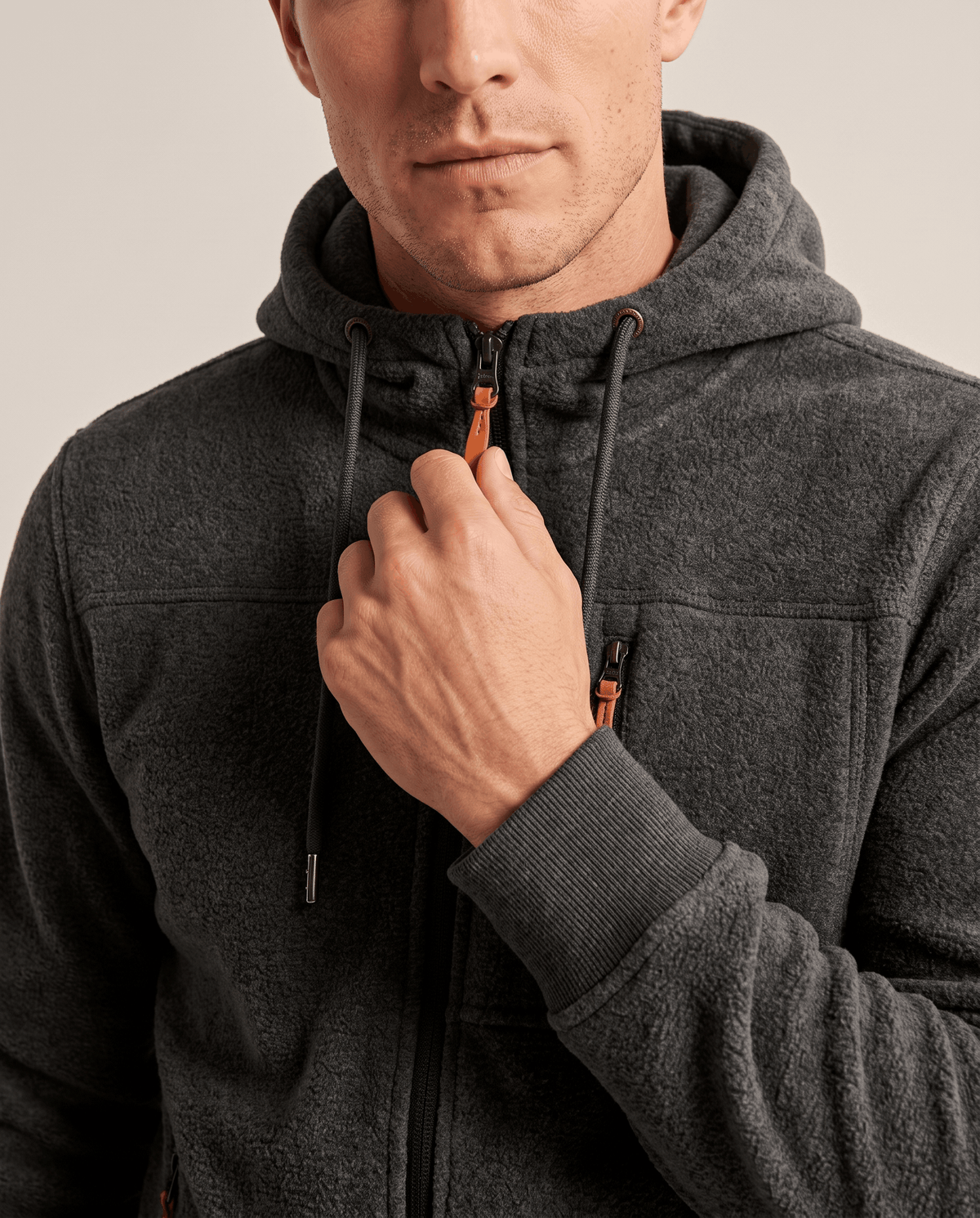Close-up of a hand on the zip and drawcord of the dark gray hoodie