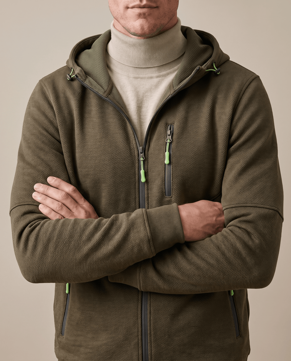 Olive hoodie with neon zip pulls worn over a cream turtleneck