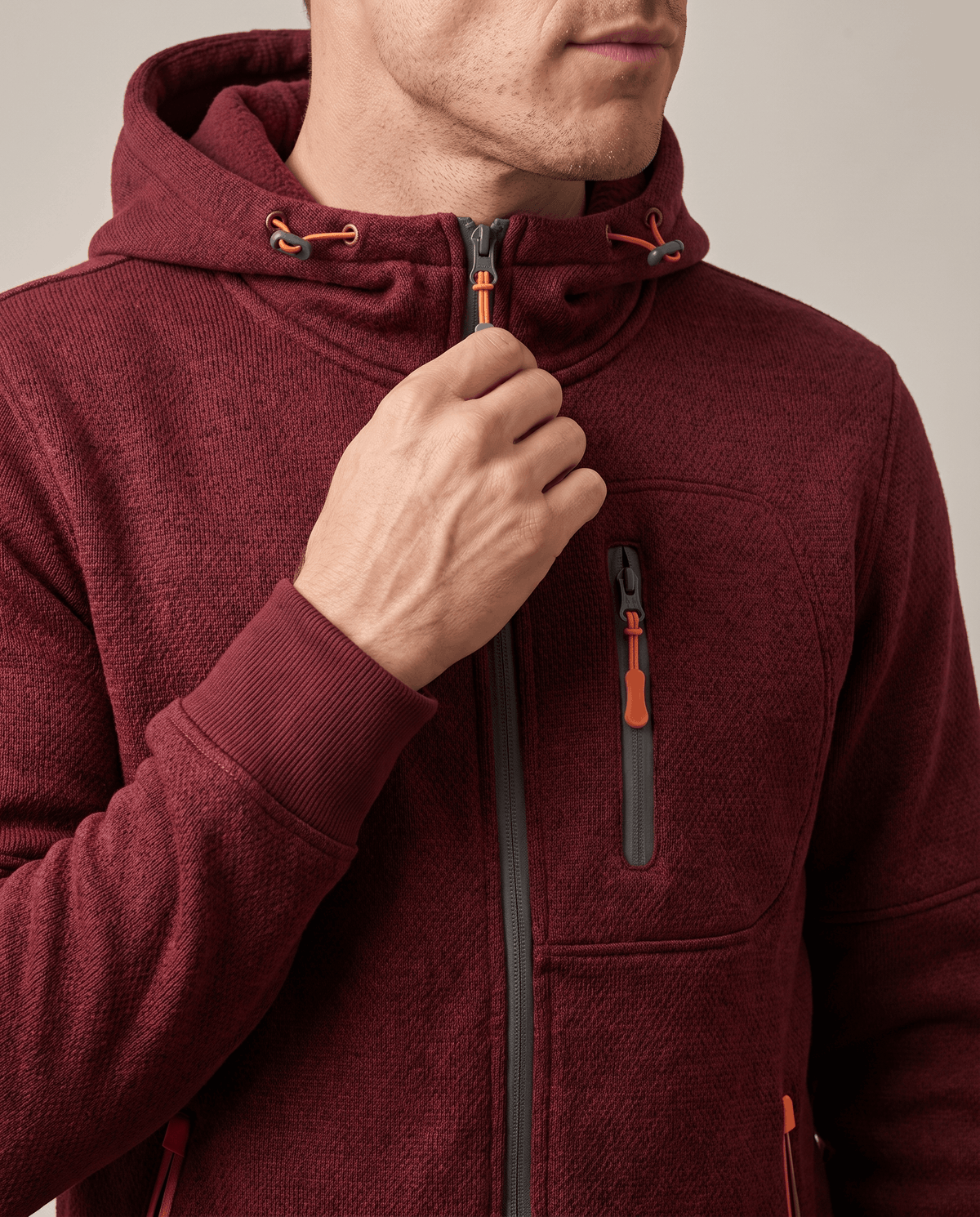 Close-up of a hand on the zip of the red hoodie near the drawstring hood
