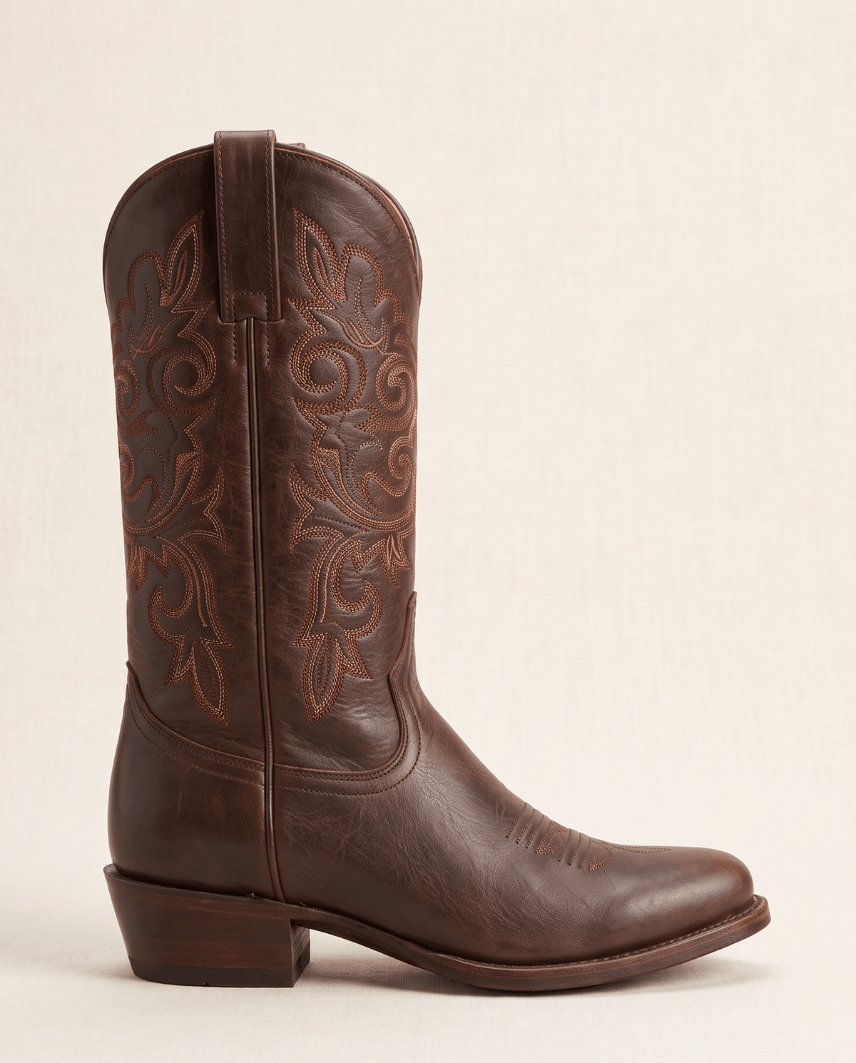 Side view of a single brown boot showing round toe, embroidered shaft and stacked heel