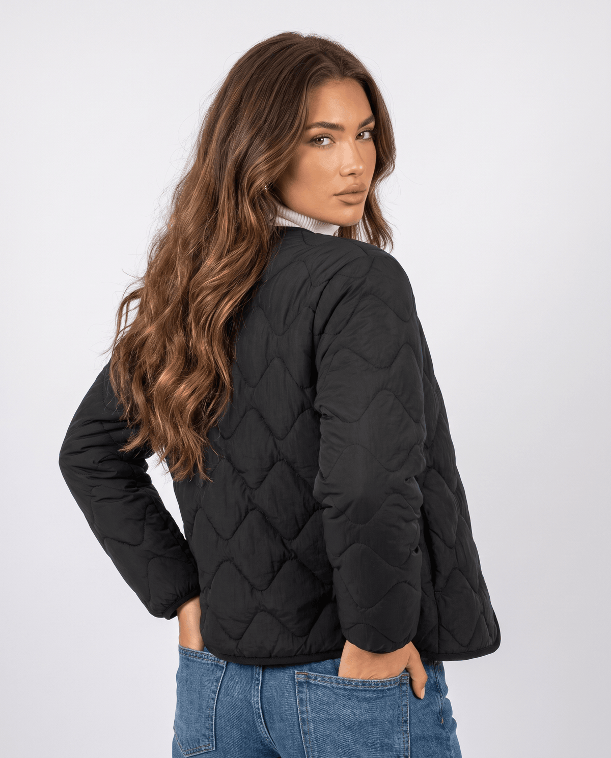 Back view of black quilted jacket worn with white turtleneck and jeans