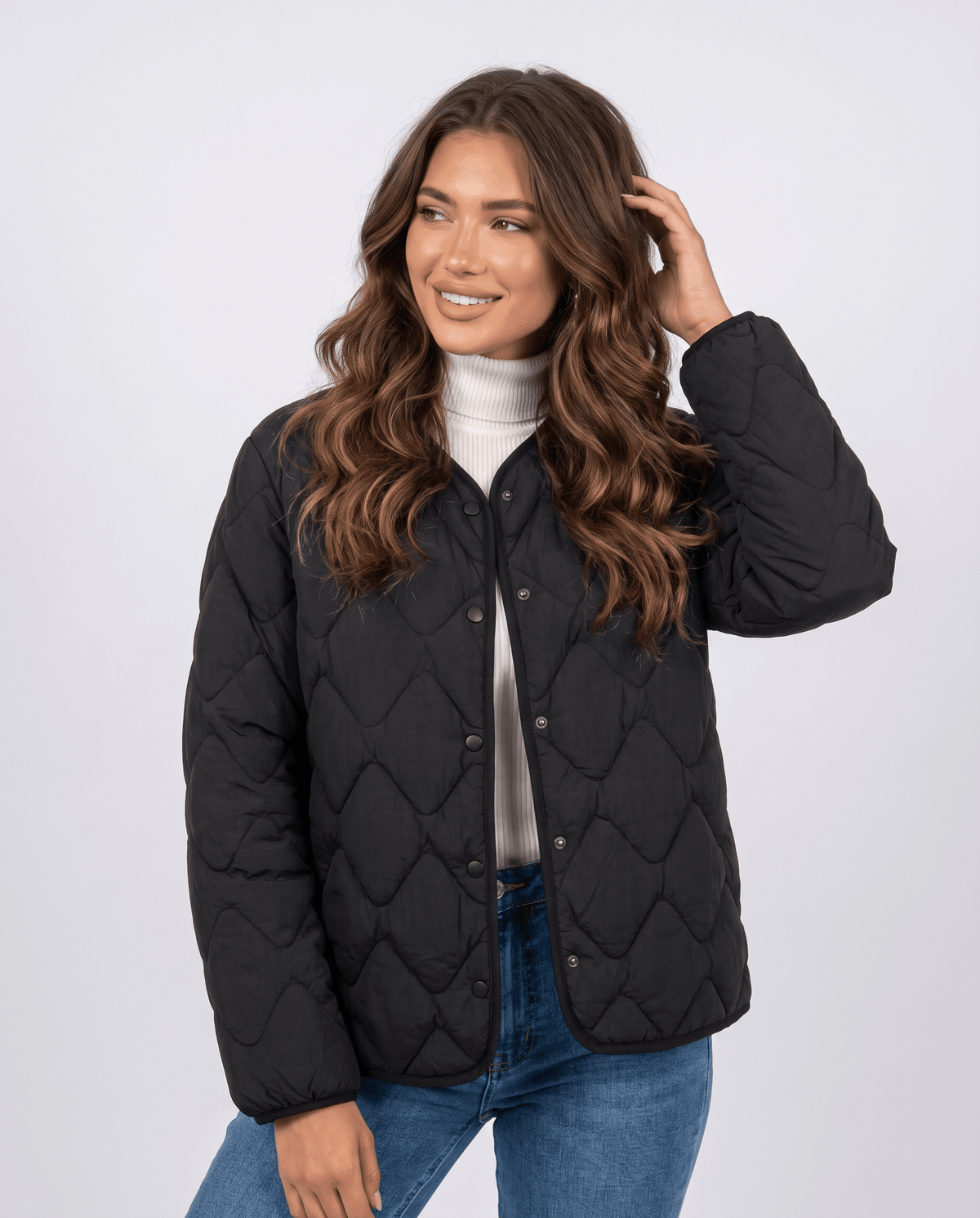 Model in black quilted jacket with snap buttons over white turtleneck, hand in hair