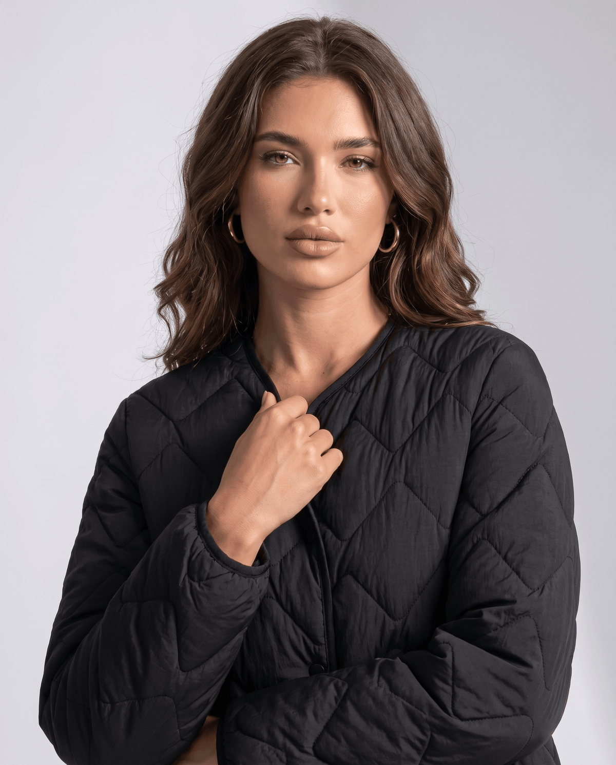 Close-up of model with hand at black quilted jacket neckline, front view