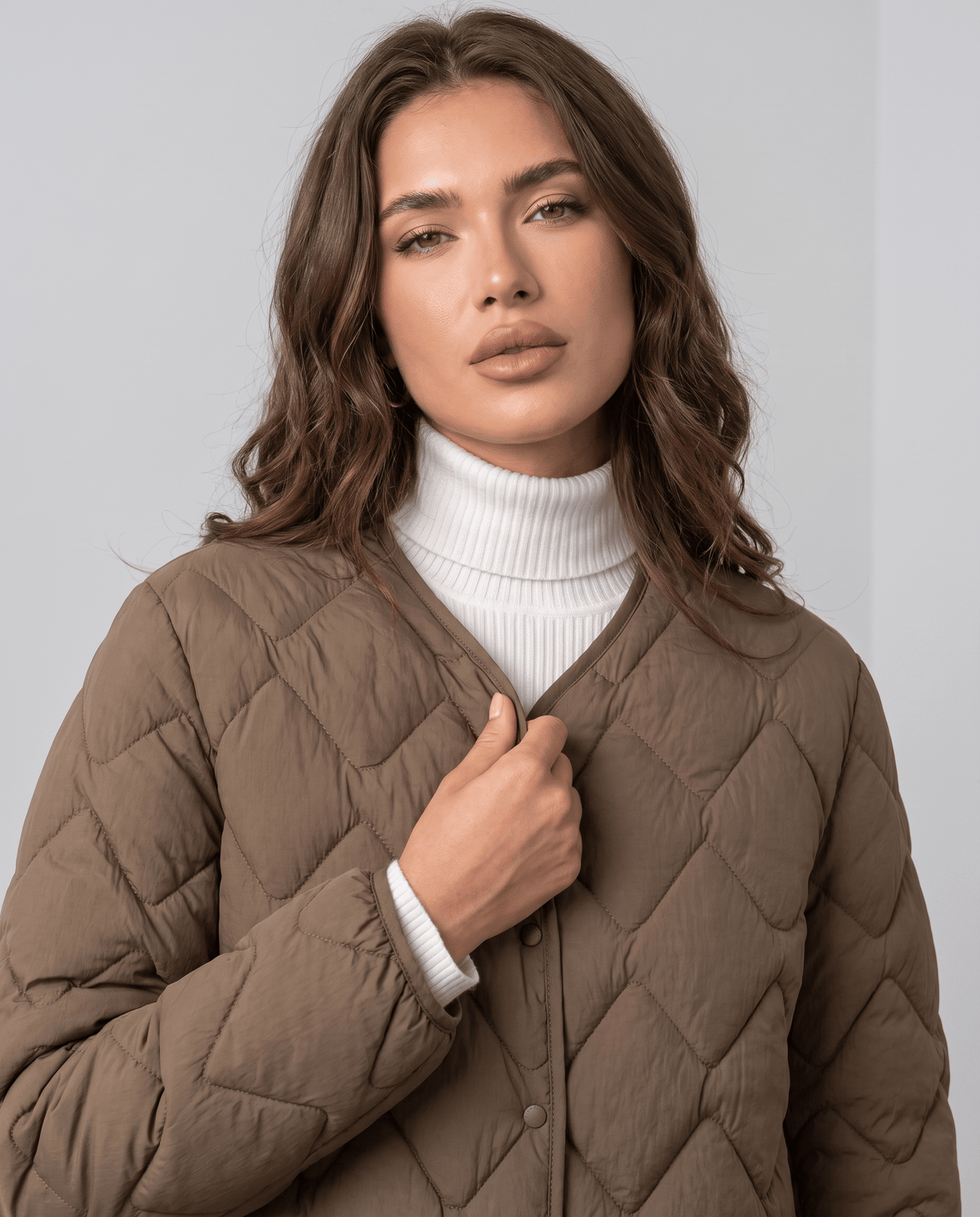 Model in brown quilted jacket with hand at the snap placket over white turtleneck
