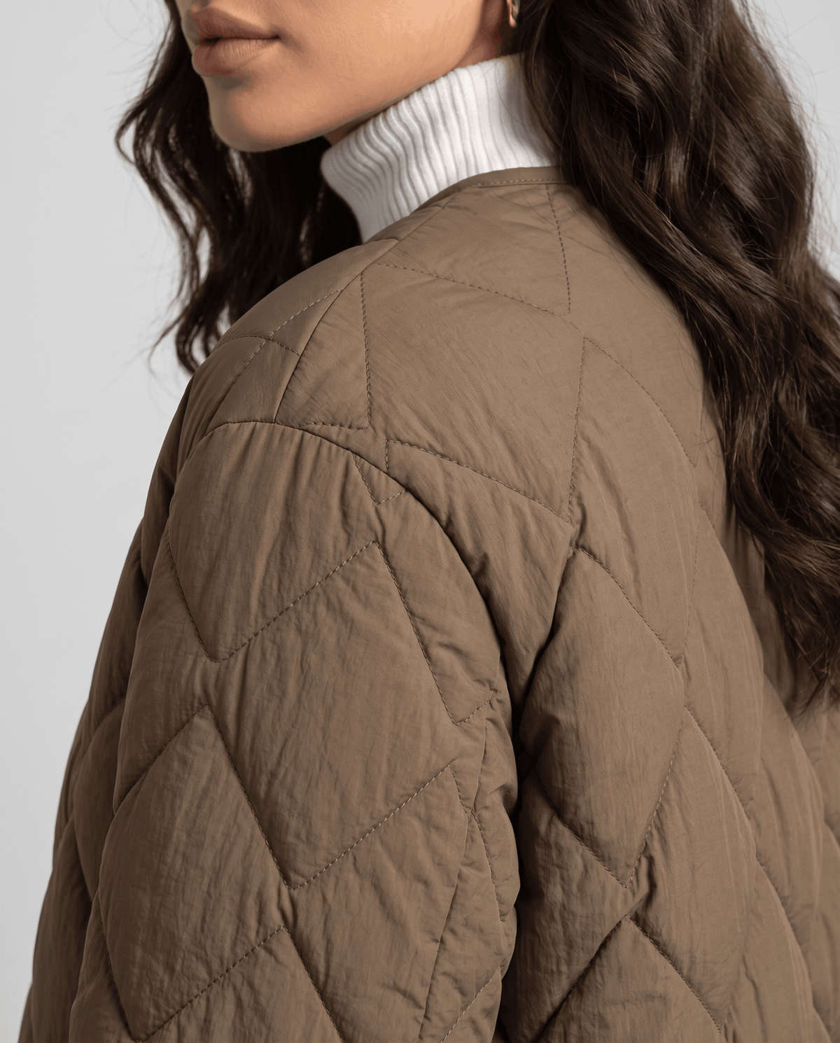 Close-up of brown diamond quilted shoulder and sleeve over white turtleneck collar