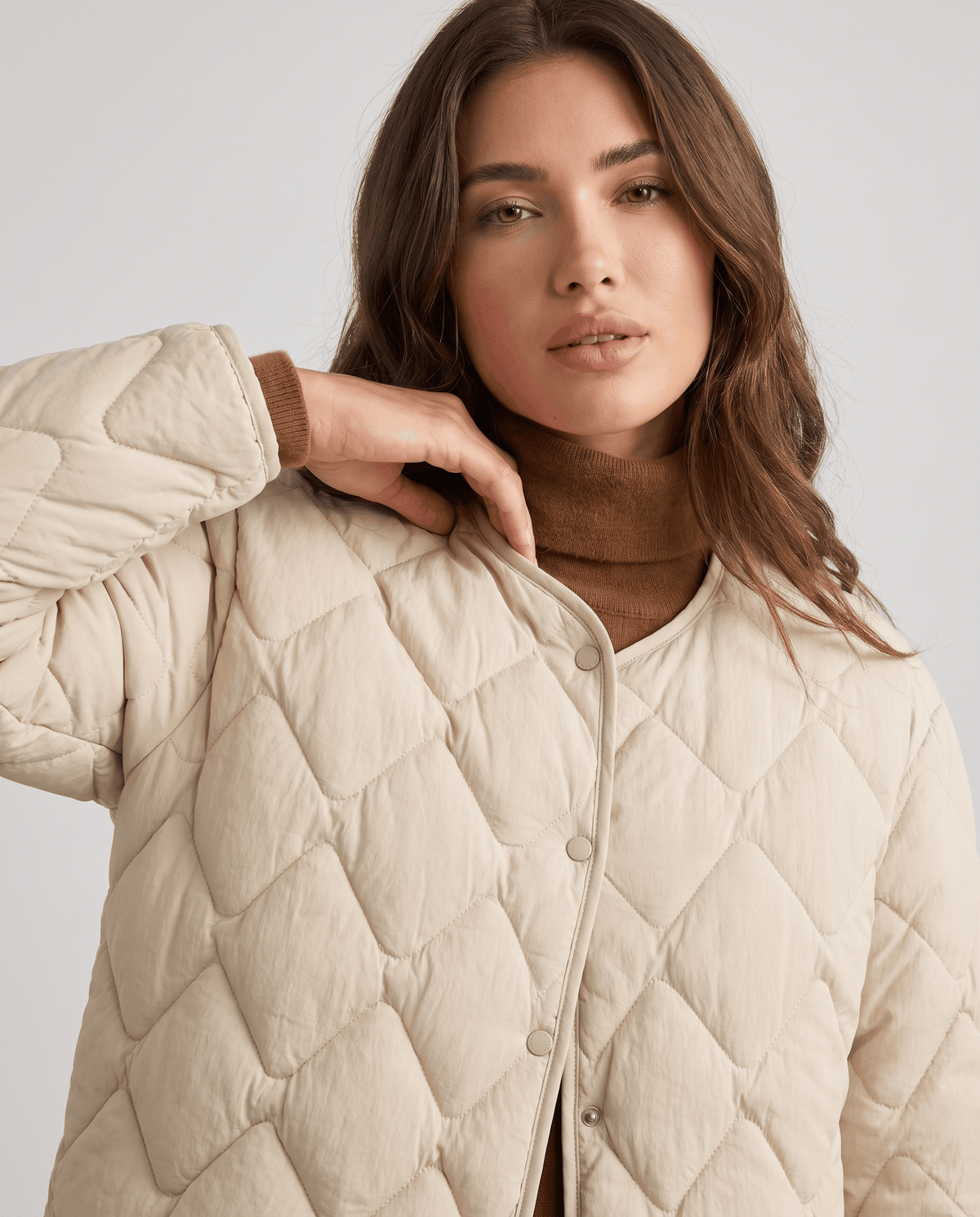 Close-up of cream quilted jacket with snap buttons and collarless V-neck over brown turtleneck
