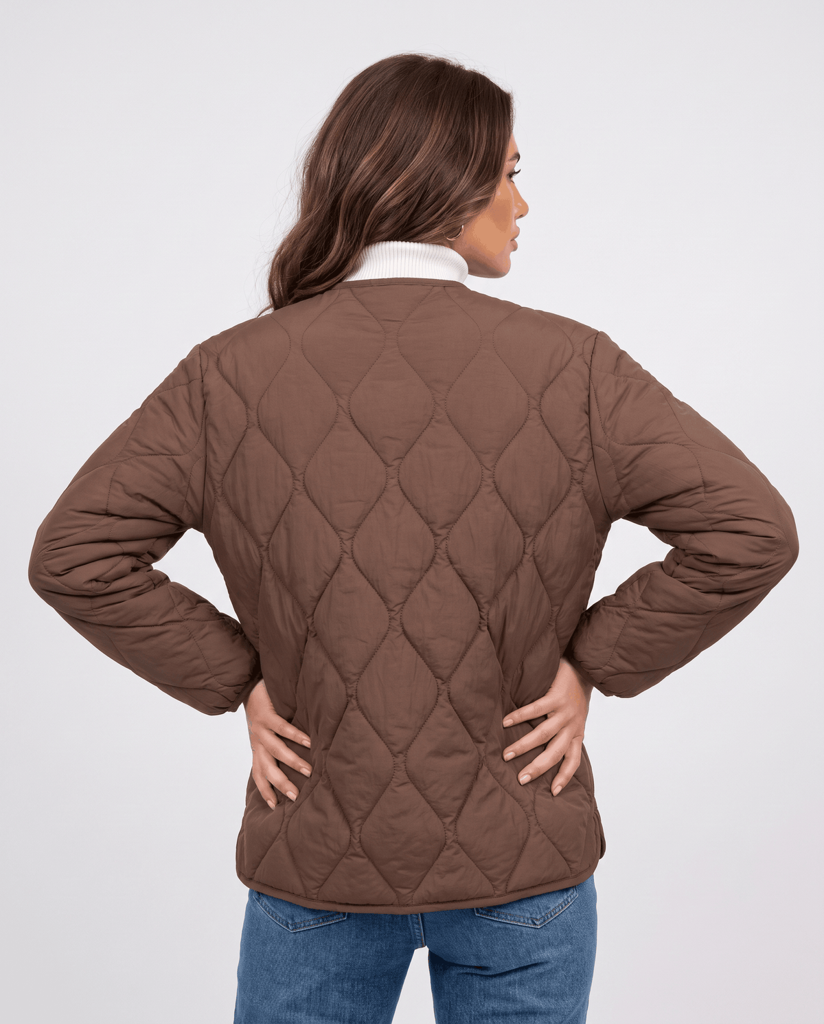 Back view of dark brown quilted jacket with hands on hips over white turtleneck