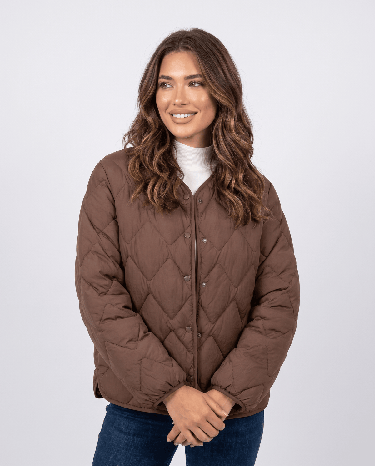 Model in dark brown quilted jacket with snap front and collarless neckline, hands together