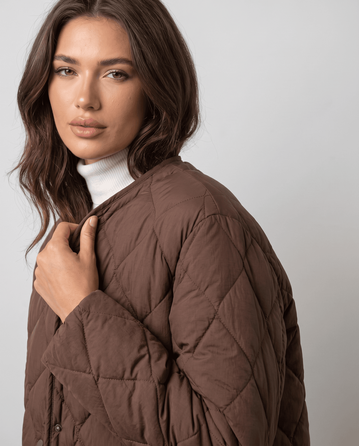 Close-up of model with hand at dark brown quilted jacket neckline over white turtleneck