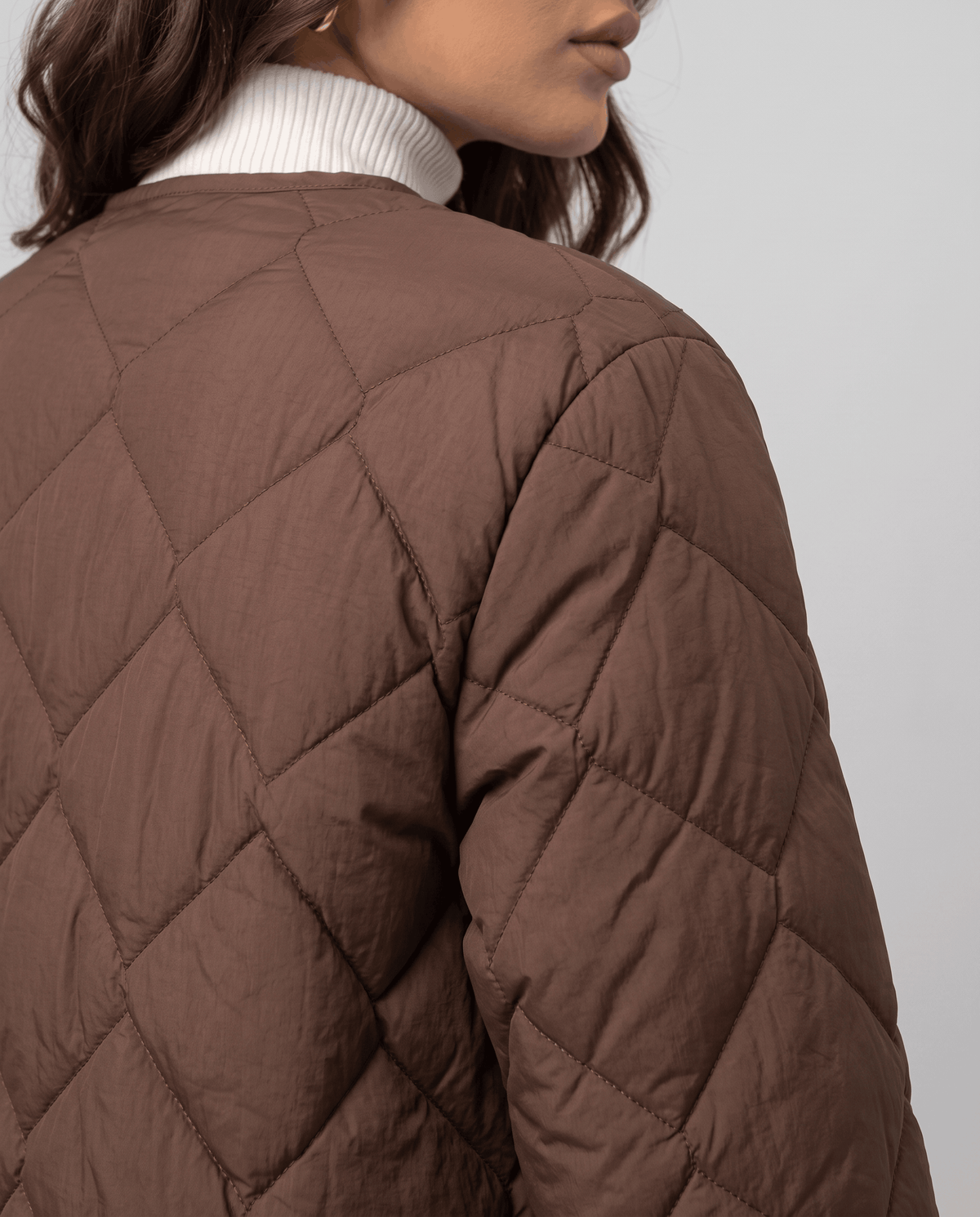 Close-up of dark brown diamond quilted shoulder and sleeve over white turtleneck