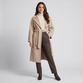 Woman in beige long belted wrap coat over a cream turtleneck and brown trousers