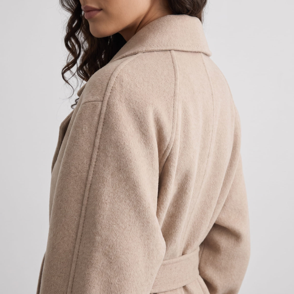Rear shoulder detail of beige coat showing the dropped shoulder seam and belt