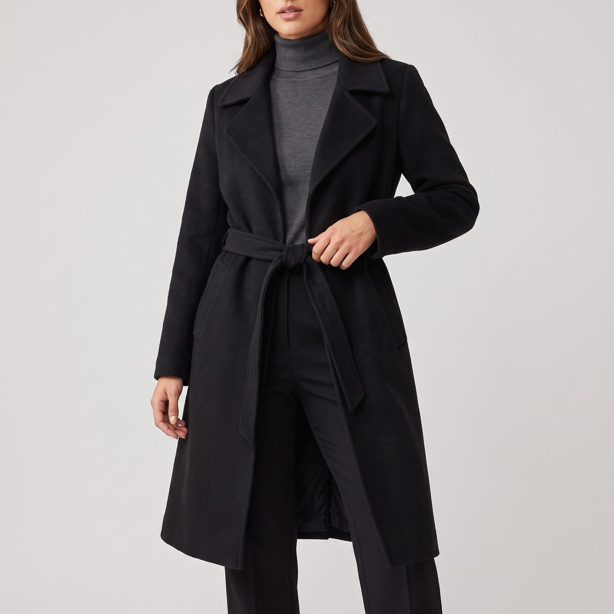 Black coat tied at the waist over a gray turtleneck and black trousers