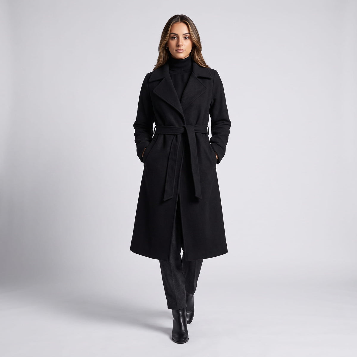 Model walking in black coat belted at the waist with black ankle boots