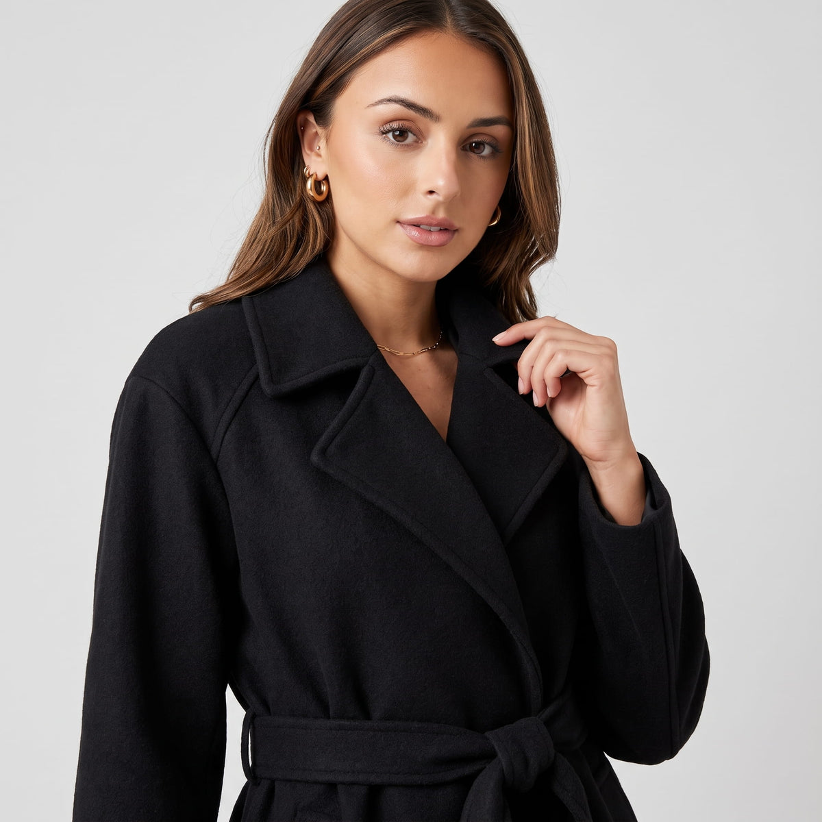 Close-up of model touching the notched lapel of a black belted coat