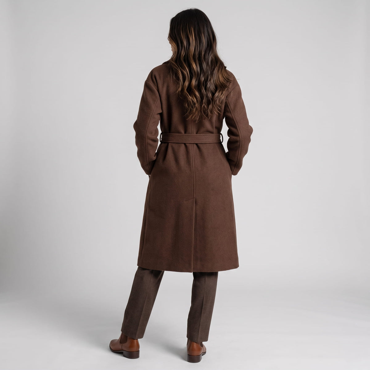 Back view of brown coat with belted waist over dark trousers