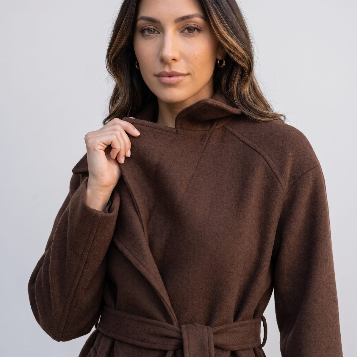 Model holding the collar of a brown coat, close-up with belted waist