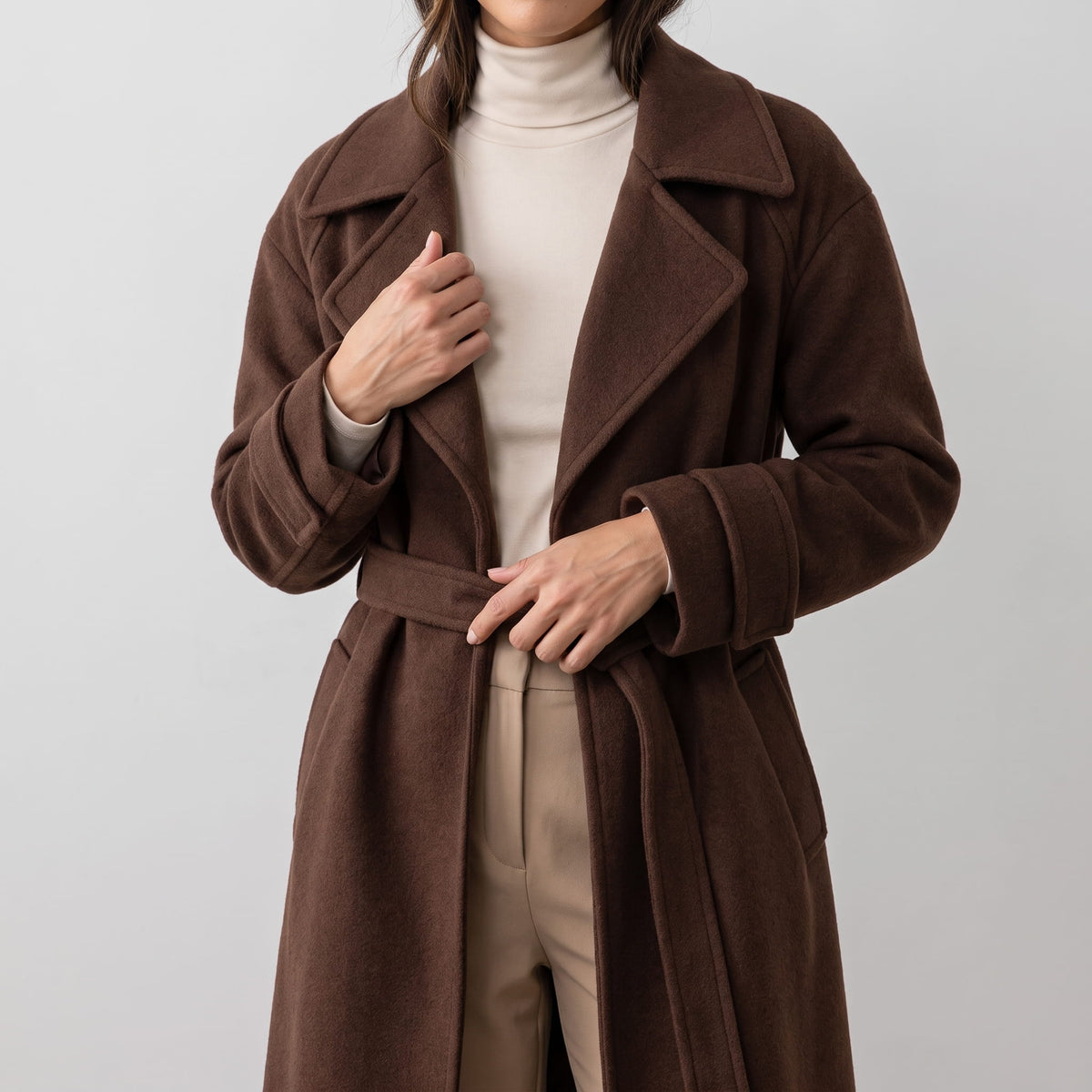 Brown coat worn open over a cream turtleneck with the belt hanging loose