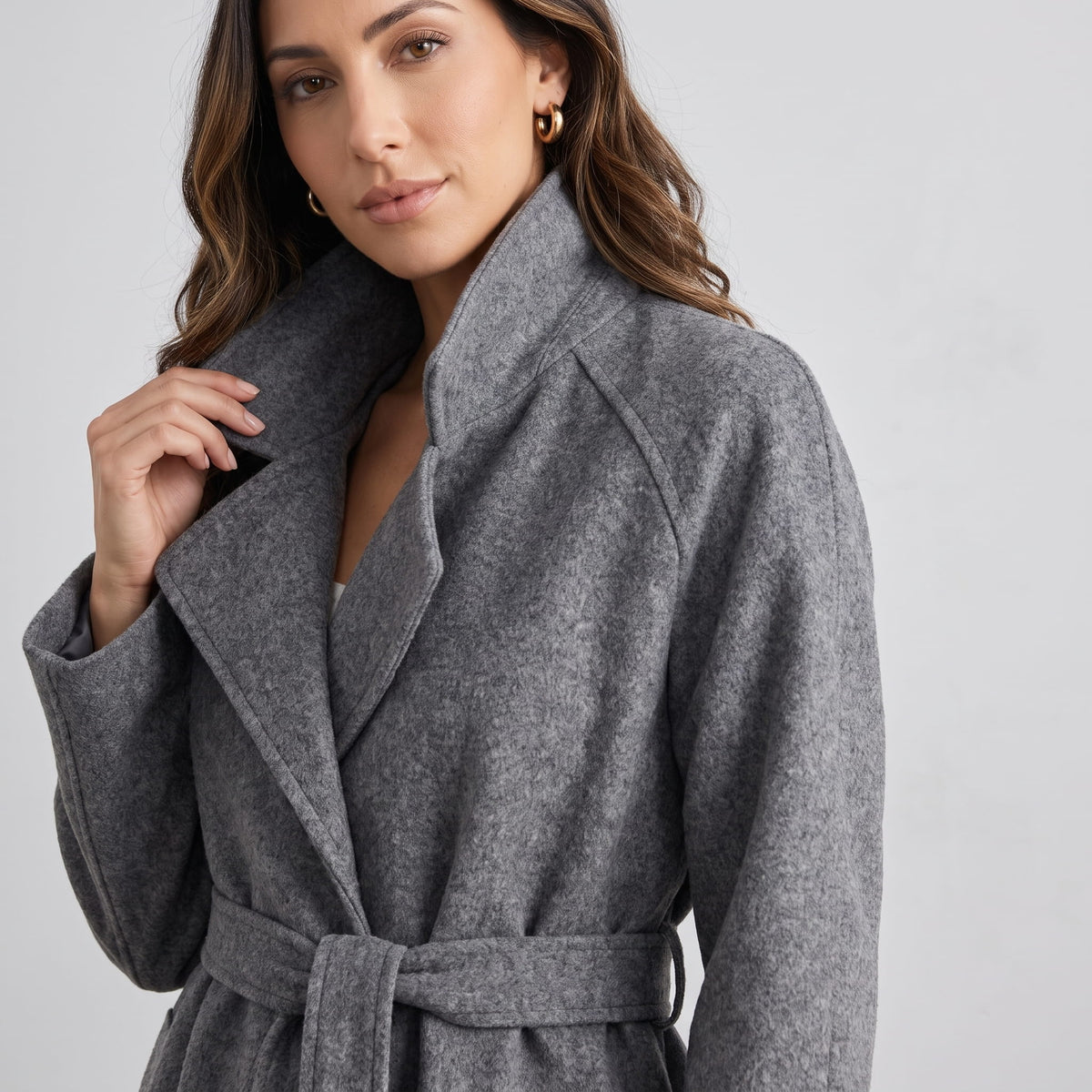 Close-up of model holding the lapel of a gray coat tied at the waist