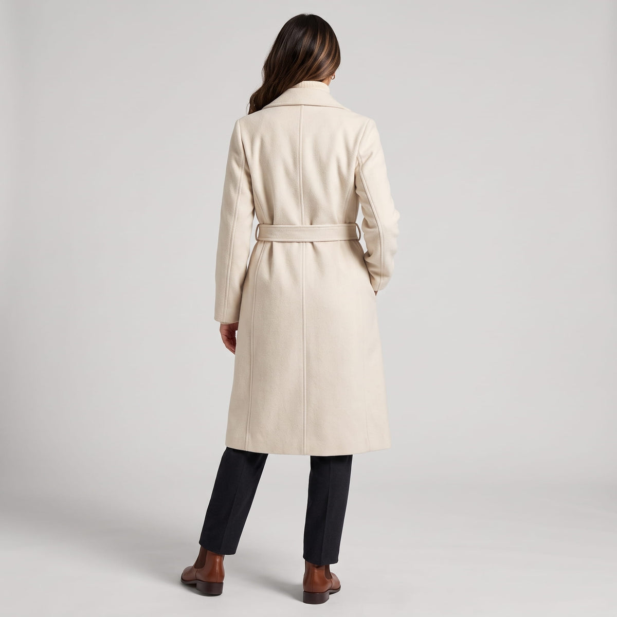 Back view of off-white coat with belted waist over black trousers