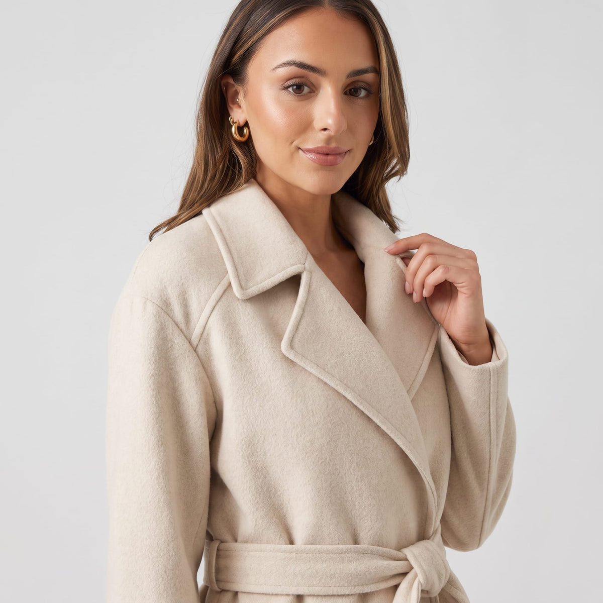 Close-up of model touching the notched lapel of an off-white coat