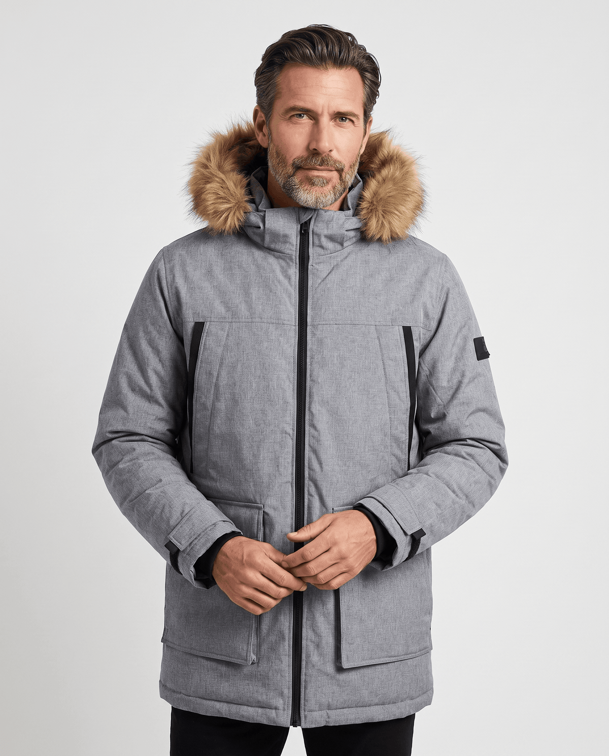 Man wearing a gray long hooded parka with full-length zip, hands clasped at the front