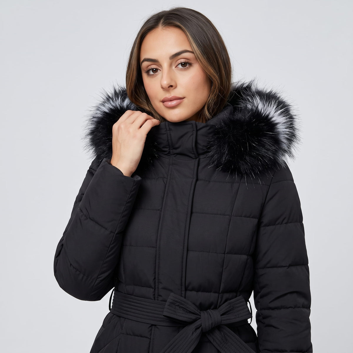 Model holding the collar of a black belted puffer coat