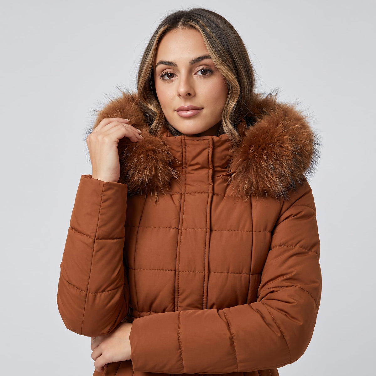 Model holding the plush hood trim of a caramel puffer coat