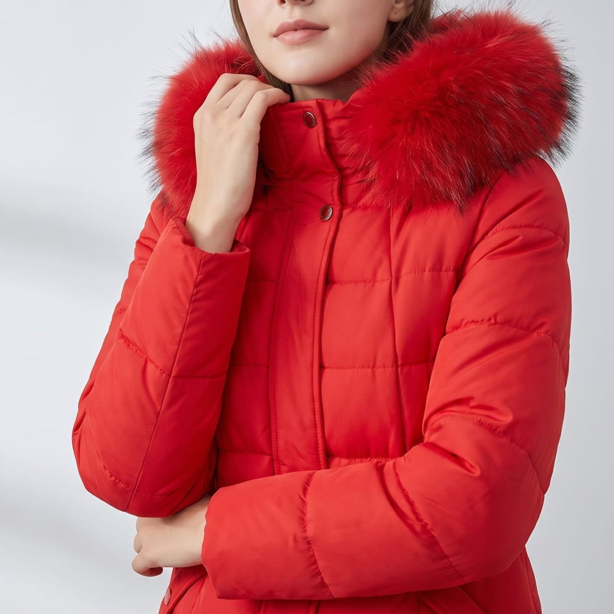 Model touching the red plush hood trim of a quilted coat