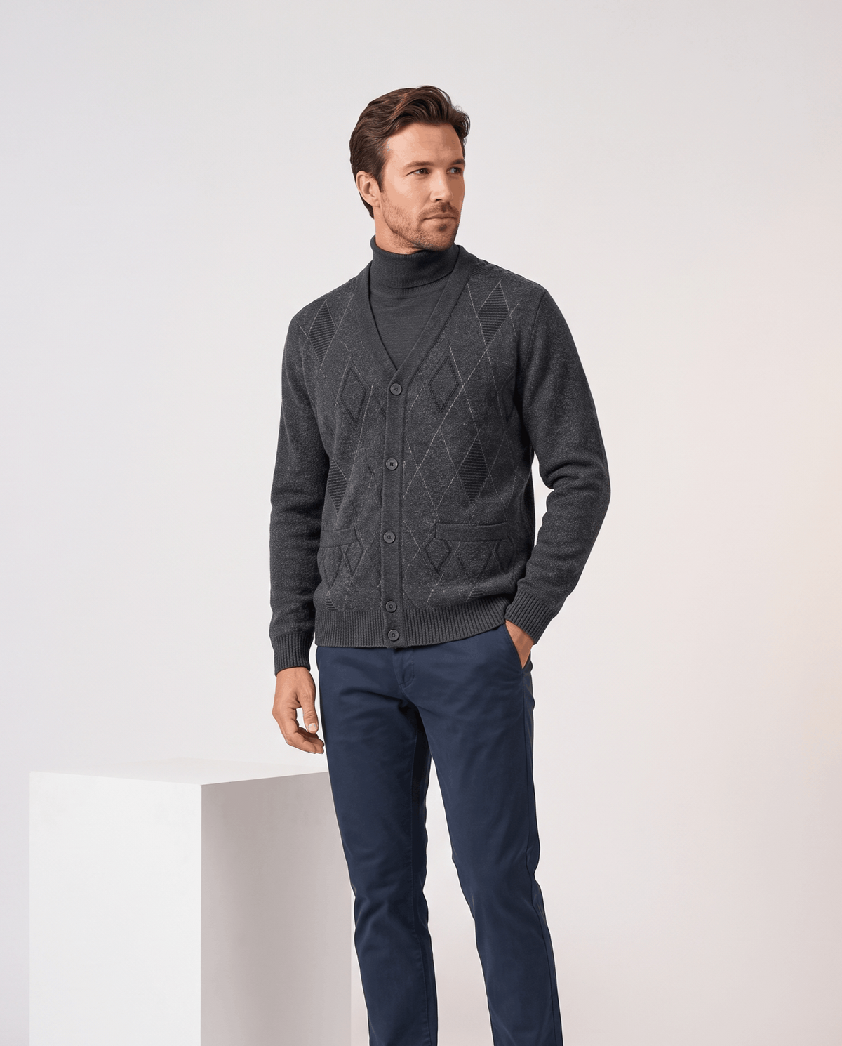 Man wearing a dark gray argyle cardigan buttoned with one hand in his pocket