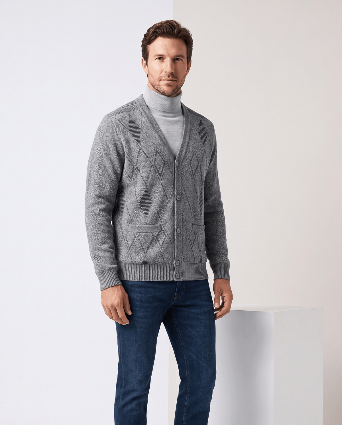 Man in a light gray argyle cardigan over a gray turtleneck and blue jeans