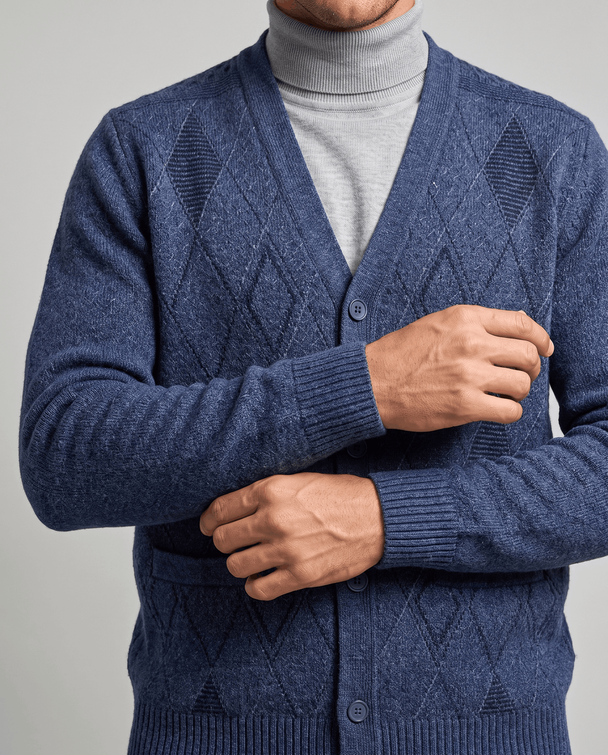 Close-up of hands fastening the buttons on a navy argyle knit cardigan